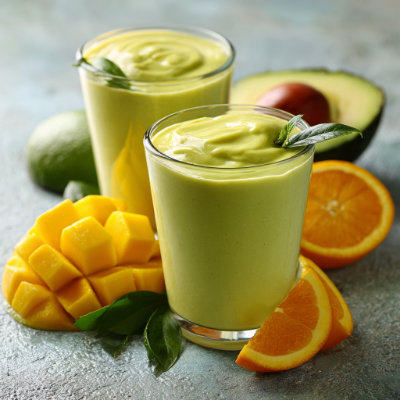 A creamy green and yellow smoothie in a glass with a straw, garnished with a slice of mango.