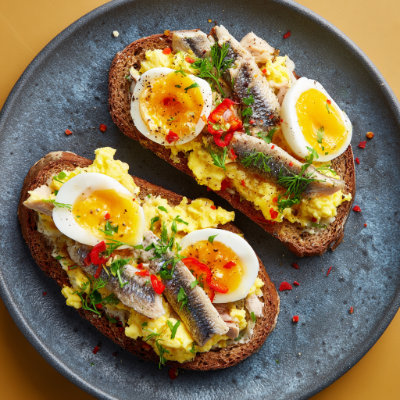 Toasted whole-grain bread with scrambled eggs and sardines, on a white background with a NutrientShield logo.