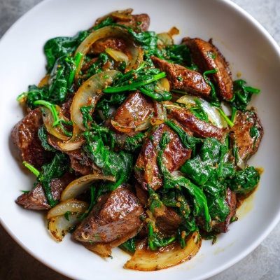 A skillet dish with beef liver and spinach, on a white background with a NutrientShield logo.