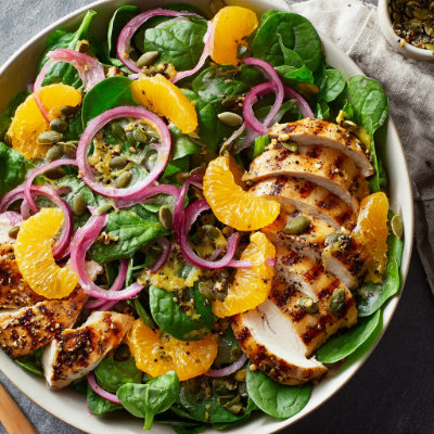 A bowl of fresh spinach salad with grilled chicken, pumpkin seeds, and a light dressing.