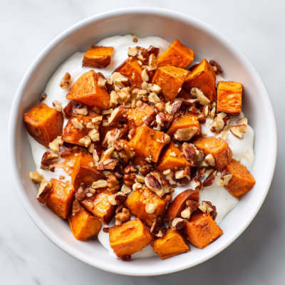 A bowl of roasted sweet potato cubes with nuts and yogurt, on a white background with a NutrientShield logo.